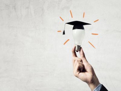 Hand holding lightbulb with graduation cap on top