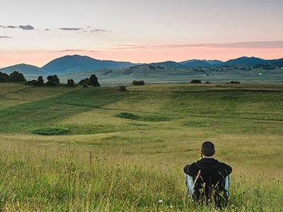 man sitting in field looking at mountains