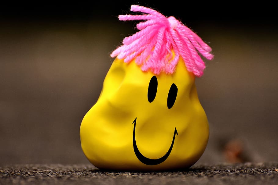 A yellow balloon with a smiley face on it with pink string coming out of the top to make it look like hair