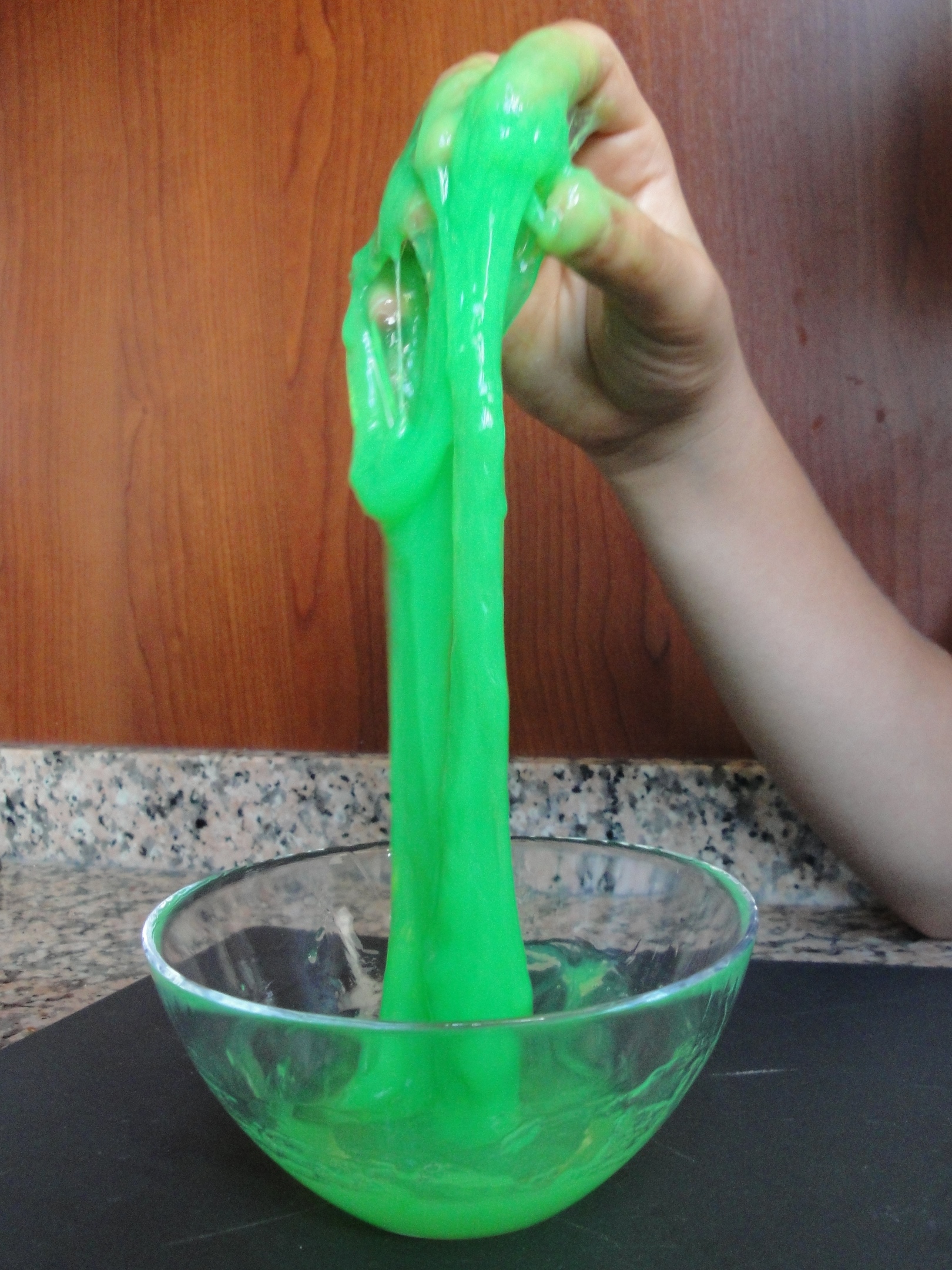 A hand holding green slime coming out of a clear bowl