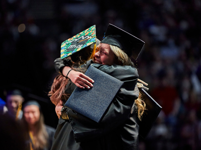 Students hugging in their graduation attire to celebrate Commencement