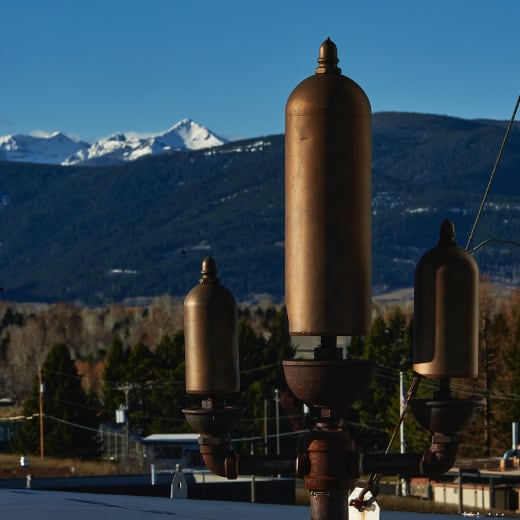 A steam whistle on top of a building with mountains in the background.