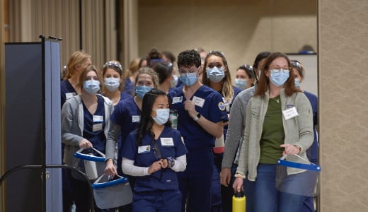 A group of people in nursing scrubs walks through a wide doorway.