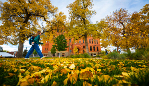 A woman walks along a sidewalk on a college campus in autumn.