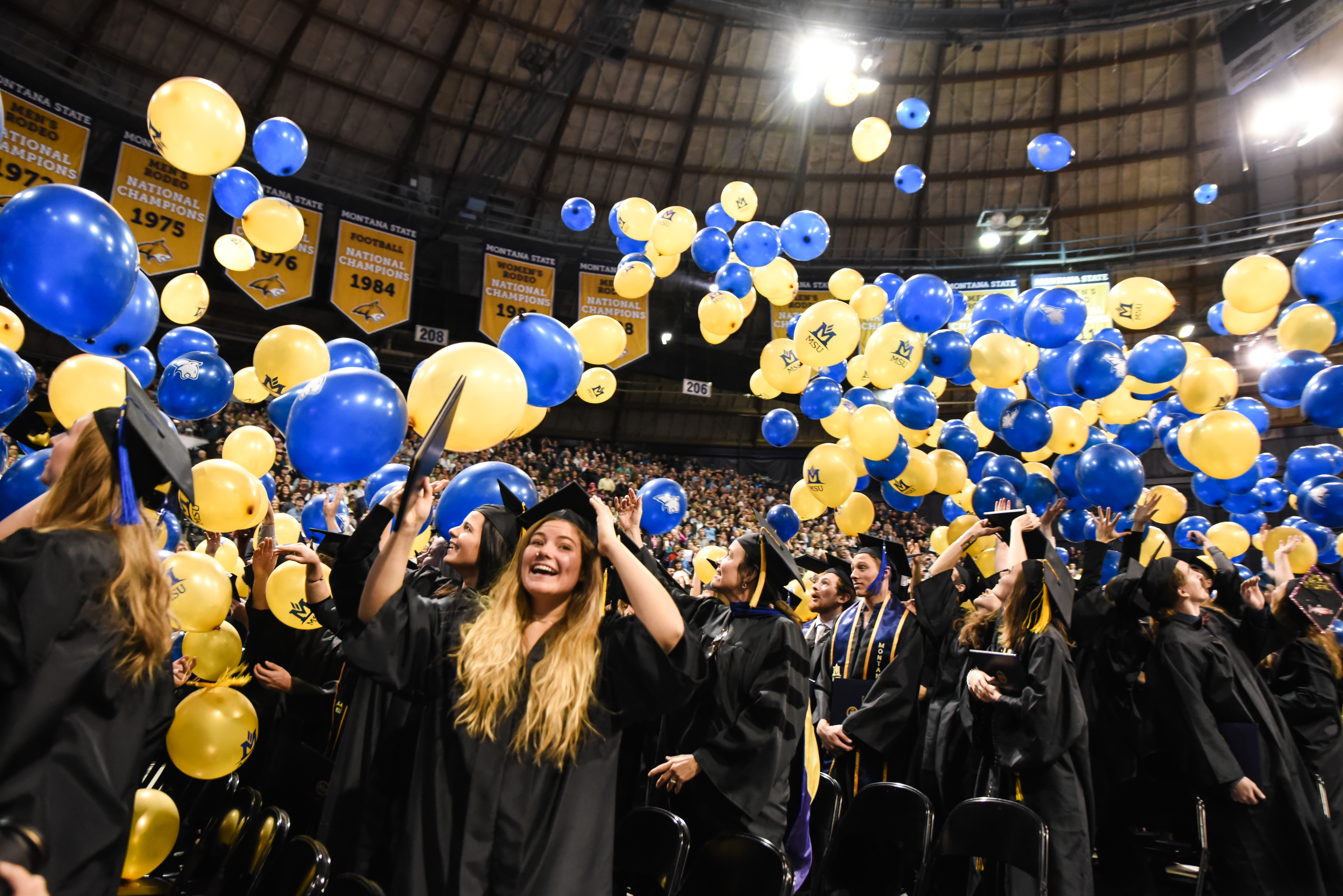 woman in graduation regalia underneath balloon arch