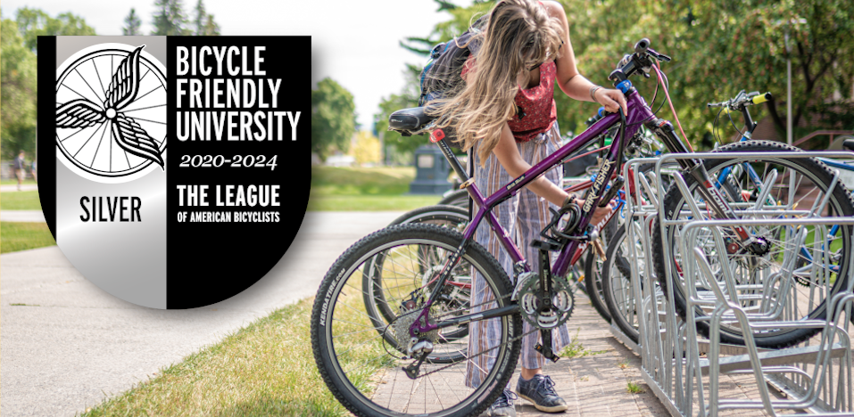 A student uses a bike rack next to the silver Bike Friendly University seal