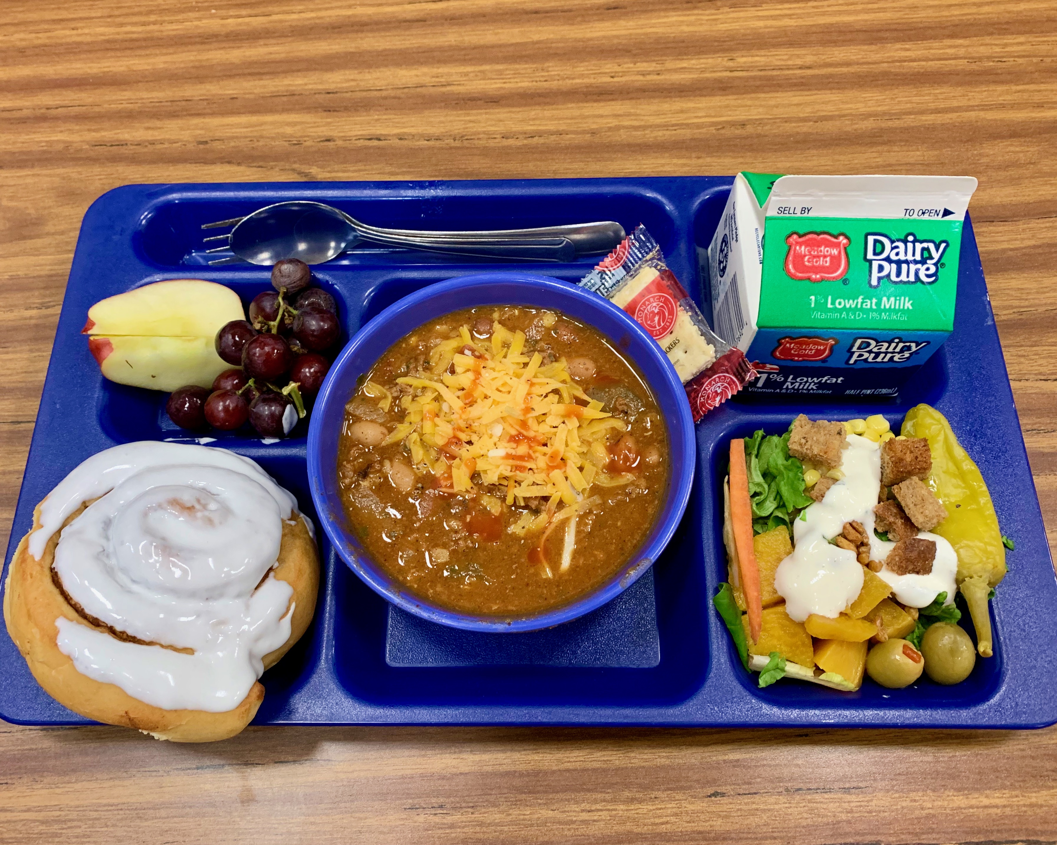 school lunch tray with chili, salad, fruit, milk, cinnamon roll