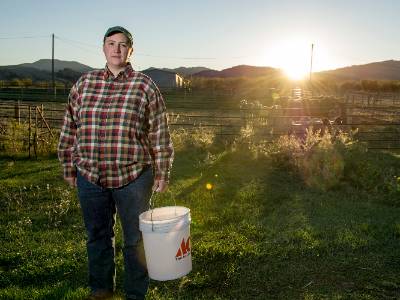 Michelle Knerr holding a white bucket in front of lambs at sunset