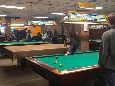 Rec Center Students playing pool in the SUB Rec Center. A girl is taking a shot, while a boy watches.