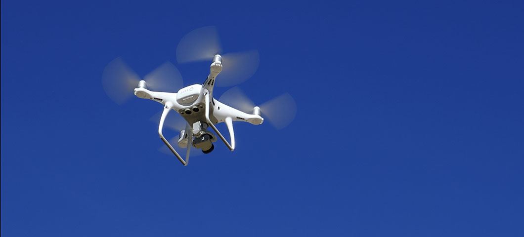 A small UAS or drone flying against a blue sky.